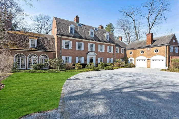 On the eastern shore of Hempstead Harbor, this grand 1920 brick Dutch Colonial manor commands serene vistas of the harbor’s cerulean waters and its emerald lawns edged by towering trees. Oh, the tales this historic home could tell us of summer soirees held in her garden-like ballroom or of intimate winter gatherings where friends could relax and chat after dinner in front of one of her many inviting fireplaces. Though well-cared for nearly a century of existence, this grand lady is ready for you to give her the facelift she deserves so she can serve you well in this new millennium. With steps down to the water, deck, and deck shed, an expansive stone patio, attached two-car garage, high ceilings, elegant moldings, twelve-over-twelve windows galore, six bedrooms, six full and two half baths, not to mention a servant’s wing, she has much to offer. Approached by a long tree-lined drive off a private road in the fabled “Gold Coast” community of Roslyn Harbor, she shares a rich heritage with her neighbors. A farming community originally, Roslyn Harbor was developed by wealthy New Yorkers in the early 1900’s, into their summer estates.  Two of those properties remaining today are the Engineer’s Country Club and the William Cullen Bryant Preserve with the Nassau County Museum of Art.  Located just north of Roslyn Village, the area is convenient to shopping (including the Americana at Manhasset), dining, golf, boating, beaches, equestrian facilities, and the railway station. It is about 45 minutes from Manhattan by car or rail.   
With a large bluestone pebble courtyard, gambrel roof, and attached two-car, carriage-house-like garage, this stately brick Georgian manor seems to welcome you with open arms. Her center-hall entrance foyer, with its graceful floating staircase, cloak and powder rooms, and fireplace, extends to the rear of the house with door to the patio. To the left, a generous living room with front and rear windows offers fielded-panel walls, hardwood floors, fireplace, and four corner built-in display cases, with doors opening to the garden room. This ballroom-sized space is the gem of the home where stone floors flow through several sets of French doors with fanlights. At one end is a grand fireplace, and at the other, a walk-in bar. To the right of the foyer, the banquet-sized dining room displays a magnificent fireplace at one end and a wide, arched niche at the other. A swinging door opens to the eat-in kitchen, with backstairs up to the second floor, and its sunny breakfast area with terracotta tile floors and brick fireplace. A service area provides access to a powder room, laundry, the garage, and a side entrance.
The second and third floors offer great potential with a palatial master suite, featuring a huge sunny bedroom, fireplace, dressing room with built-ins, closets, and two master baths. A long hall broken up by occasional arches, closets, and service rooms, leads to three bedrooms with baths en suite, the back stairs, and access to the housekeeper’s quarters, and to the servants’ quarters in the walk-up third floor and above the garage. All offer a great potential to transform and use as you wish, as does the basement with outside entrance and ample space for storage. If you love the history of Long Island’s “Golden Age,” and long for waterfront property in a great location, this beautiful century-old residence will be an answer to your dreams and a canvas on which to paint them.
