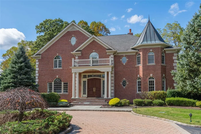 If you love the majesty and romance of Long Island’s “Golden Age” estates, with their grand mansions and sprawling arboretum-like acreage, but are seeking something more manageable in size, then this magnificent four-bedroom, five-and-a-half-bath home, ensconced on over two spectacular acres, may be the answer to your dreams. Providing charm and beauty like that of Old Westbury Gardens (a museum estate built in 1906), only a few thousand feet away, it additionally offers new millennial state-of-the-art amenities and a light and airy style so desirable today. Located on a gentle rise off a winding cul-de-sac court in Old Westbury, it is in the heart of Long Island’s fabled “Gold Coast. Long a popular area for Manhattan’s magnates and luminaries, Old Westbury is just 30 minutes by railway or highway from Manhattan plus Kennedy and LaGuardia airports.  Conveniently located near parks and museums, it is just a short drive from fine dining, premier shopping, country clubs, miles of public equestrian trails, polo club, yacht clubs, universities, and beaches.
Approached through grand iron gates, electronically controlled, and up a winding drive to a spacious circular courtyard, this stunning 2003 brick Colonial offers a continental, if not royal presence with gables accented by dentil moldings, coined corners, and a metal-roof turret. An imposing portico frames a romantic arched double-door entry accented by floral carvings, which are echoed in its leaded-glass side and transom lights. Set back on two acres of masterfully designed landscaping that create the illusion of being a much larger property, this magical residence is the quintessential entertainer’s paradise. A walkway from the front courtyard wends its way past estate fencing to an immense rear paving-stone patio that enfolds a large Roman-style, Gunite, saltwater pool with attached spa and waterfall, all surrounded by flowering shrubs, specimen plantings, and a backdrop of lush towering trees. At one end, an expansive raised bluestone terrace, extending the width of the house, includes an outdoor kitchen with built-in grill and refrigerator. It overlooks the pool and beyond to stone walls and massive steps ascending to the enchanting upper lawn.
The home’s interior is no less impressive beginning with its bright and sparkling two-story foyer. Featuring radiant-heated white marble floors and a graceful bridal staircase with filigree balustrade, it proffers massive crown molding and fielded-panel wainscoting that flow through a wide archway into a sunny formal dining room. Sunlight entering through a Palladian window dances across the inlaid oak floors in this banquet-sized space. French doors open into the kitchen. The rear foyer leads to the spectacular two-story living room flooded with sunny views of the rear property through three sets of French doors beneath a soaring Palladian-style window. Offering inlaid oak floors and a second-floor balcony, this inviting gathering place invites you to sit and relax in front of a large fireplace with overmantel television flanked by built-in bookcases. 
Also accessed from the living room and rear foyer, the delightful and spacious French Country kitchen is a cook’s delight with extensive granite-topped cabinetry and generous center island with seating, wine cooler, prep sink, and an integrated Miele dishwasher. A second Miele dishwasher adjoins an undermount double sink beneath a large bow window, ideal for potted herb garden. Additional appliances include a huge refrigerator/freezer with two doors and four drawers, a six-burner-and-griddle Viking cooktop with pot filler, double-oven, warming drawer, and General Electric microwave. Beautiful porcelain floors flow into a sunny breakfast alcove overlooking the pool while arched French doors open to the patio and outdoor kitchen.
Off the rear foyer, a hall, with powder room and closet, leads to a sunny and spacious guest suite on the right, with large bay window, oak floors, and charming full bath, and an impressive cherry-paneled study on the left. This roomy retreat boasts a coffered ceiling, built-in cabinetry, a cozy gas fireplace, plus arched French doors opening to the rear patio. Accessed from the foyer, the full finished basement includes a comfortable home theater, a full bath with shower, a storage and utility area, mudroom opening to the attached, heated three-car garage, and, on the other side of the house, access to wide steps leading to the patio and pool area.
On the second floor, off the hallway balcony overlooking the living room, the palatial master suite, in a wing of its own, will enfold you with serene luxury, from its spacious bedroom with study alcove, backlit tray ceiling, built-ins with electric fireplace, and balcony overlooking the pool (a perfect spot for morning coffee), to its two walk-in closets, and a French Country spa-like bath with two vanities, dressing table, whirlpool tub, steam shower, and water closet. Also, on this level are stairs to a walk-up third floor attic, a laundry room with high-end washer and dryer, and two delightful sunny bedrooms sharing a designer bath with twin vanity and glass-enclosed tub/shower. Pristine inside and out, this amazing home appears new yet radiates a timeless charm melded seamlessly with all the amenities so sought after today. All it needs for a fairy tale ending is you.
