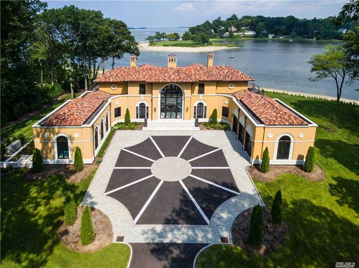LLOYD HARBOR_VILLA MARINA. As soon as one enters through its bronze gates he will be enthralled by this magnificent new Mediterranean villa, ensconced on a gorgeous property with 400-feet of shoreline. For “Villa Marina,” designed by Granoff Architects, is a one-of-a-kind masterpiece designed by those who excel at merging elements from the past with a grand vision of the future to create extraordinary residences of exquisite style and quality. Upon entering the striking front courtyard, guests will be enthralled by the dramatic arched 2-story glass entrance, tall European-style windows, wrought iron balustrades, clay Spanish tile roofing, and decorative chimney tops. On each side of the courtyard is an attached 3-car garage and a magnificent indoor pool with barrel ceiling and many arched doors and windows. This breathtaking 2-acre property is located at the entrance of Huntington Harbor and offers panoramic vistas of Huntington Bay with the Huntington Harbor Light house twinkling in the distance. Across the rear of the manse, 2 large granite verandas (one with fireplace and TV), a patio, 2nd-floor balconies and deck provide ideal vantage points for watching the many sailboats go to and from the harbor.
The interior of the home is equally impressive with high ceilings, soaring windows, gleaming hardwood floors, 5 deluxe bedrooms, 5 ½ designer baths, 4 striking fireplaces, and vintage Murano glass light fixtures. The surprising yet symbiotic use of design elements, borrowed from the early 20th Century Art Nouveau and Art Deco styles, blend seamlessly to delight the eye at every turn. Some examples are the 2-story entrance foyer’s inlaid marble floors and wrought iron filigree entrance doors and staircase balustrade.  Ideal for entertaining on a grand scale, the first floor features a remarkable living room with 2-story barrel ceiling and ornate art deco moldings, a marble dual fireplace shared with the foyer, and a tremendous 2-story box bay of solid, arched windows facing the water. Open on each side of this spectacular gathering place are a den and banquet-sized dining room, each with a wall of windows and doors opening to the rear patio. A state-of-the-art eat-in kitchen with unique stone countertops and backsplash offers a huge L-shaped center island with seating, high-end stainless steel appliances that include a 6-burner gas stove, plus a large built-in TV. Two bedrooms, 2 full baths and a powder room are also on this level.
The second floor offers 2 additional bedrooms sharing a full bath and a magnificent master suite featuring a lavish master bedroom with chandelier in its high domed ceiling, an art deco fireplace, and wall of arched French doors to a generous private deck. Also, accessing the deck, an opulent onyx master bath, offers a frameless-glass-enclosed shower with multiple shower heads, twin vanities, and a free-standing tub enjoying fabulous water views through a Palladian window. A full finished basement offers many possibilities for entertaining and storage. Come experience the quintessence of luxury “Gold Coast” living in this sumptuous, brand new waterfront haven on the eastern shore of Lloyd Harbor, with deeded dock rights, convenient to golf, equestrian and cross country ski trails, and the thriving shopping districts of both Huntington and Cold Spring Harbor villages.