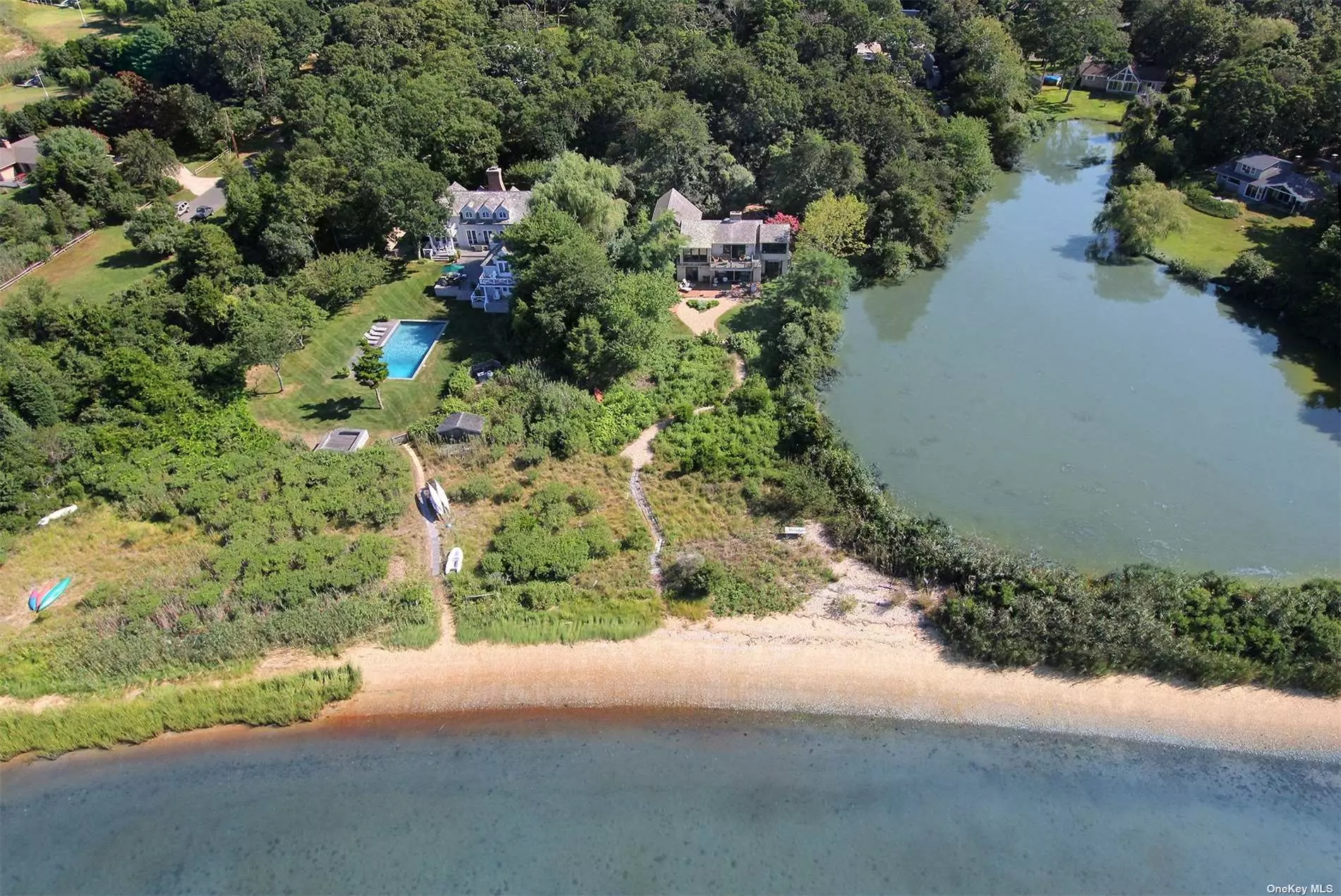 This beautiful waterfront home for sale in East Hampton features some of the best views of Three Mile Harbor and is one of the few properties with both breathtaking sunset and sunrise views. The 2, 300 square-foot house is sited on 1.2 acres and hosts four bedrooms and three baths. Exceptional details include a brick forecourt, exposed beams, expansive windows and multiple decks overlooking both an adjacent freshwater pond and the Harbor. The first floor features 2 bedrooms, one bath, a living room with brick fireplace, and kitchen with dining area. The second floor has the master suite, with the bathroom featuring a heavenly steam shower and one additional bedroom and bath. Outside, a scenic path leads to a wide sandy beach on Three Mile Harbor, where kayaks, paddleboards, and small boats can easily be launched. A unique oasis on the water with plenty of wildlife.