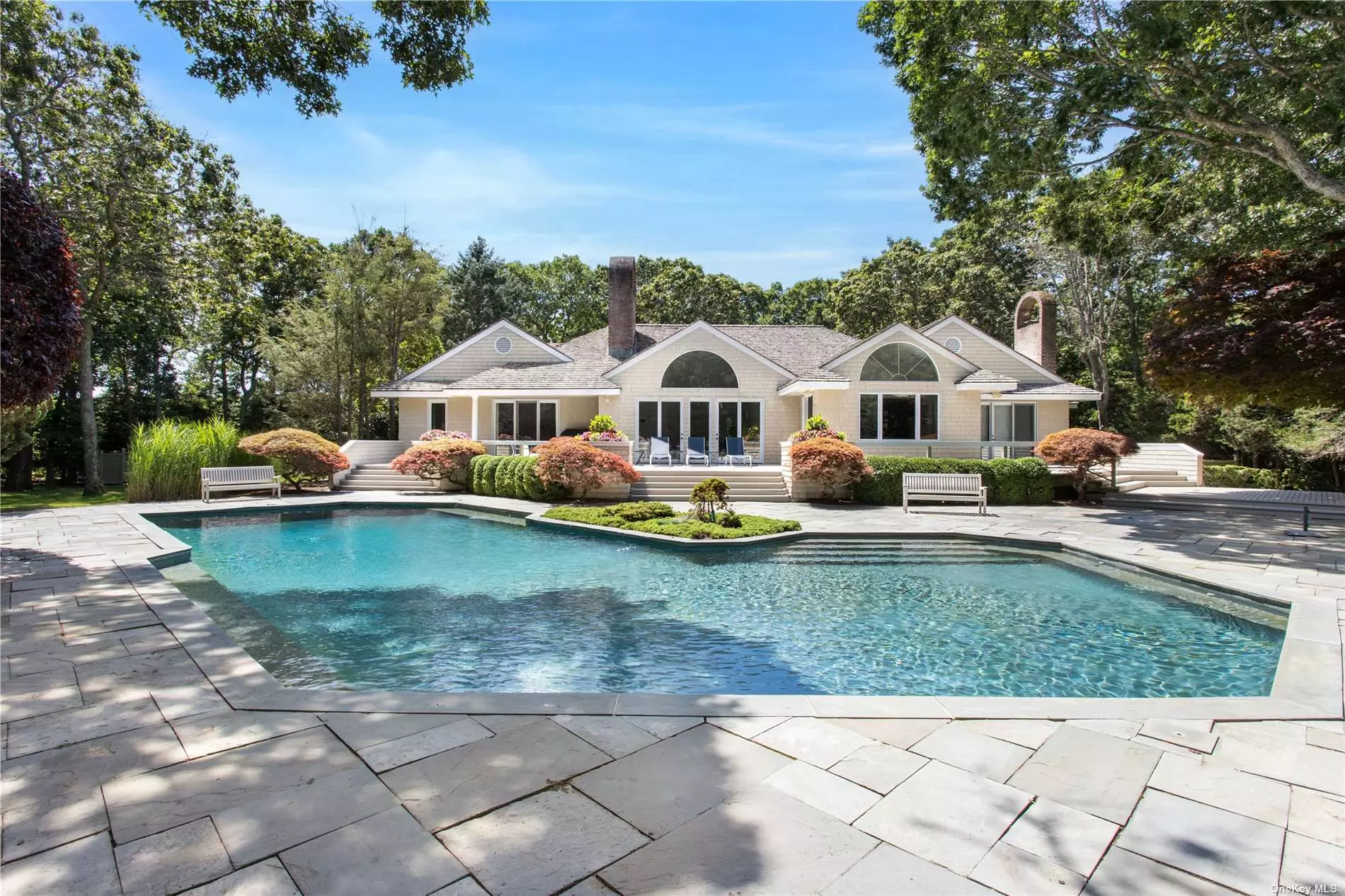 This picturesque 2 acre property and home is located at the end of a cul de sac on a country lane in the Village of Quogue. The long stone driveway leads you to the meticulously maintained mature property. The private back yard has an overly large heated gunite pool, a har tru tennis court, and a koi pond with a waterfall. There are stone pavers surrounding the pool and a large deck for entertaining. As you enter the 4, 000 sq. ft. one level home you will be in a great room with soaring ceilings and a large wood burning fireplace. From the front entry you can look out the 4 glass doors and see your secluded back yard. The kitchen has floor to ceiling cabinets, 2 stoves, 2 dishwashers, a large counter that seats six, a wet bar, and a large dining area. The principal bedroom suite is on its own side of the house with a large walk in closet, sauna and a extra large bathroom, the bedroom has glass doors that lead out to the deck. The family room with doors to the back yard can also be a bedroom it has a bathroom en - suite. There are 3 other large bedrooms with one en -suite and another full bath to accommodate the other 2 bedrooms. There is also a 2 car detached garage. This well maintained home is on the market for the first time in over 30 years, with a motivated seller, low taxes and convenient location. This should be your ideal all season luxury retreat.
