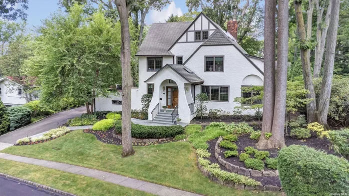 Completed in 1923 and set on a landscaped .47-acre, this well-appointed Colonial residence is surrounded by regal old growth and mature specimen trees with perennial under plantings. Perfect for relaxing and entertaining outdoors, a conveniently located terraced dining patio sits just outside the kitchen with a flagstone patio below. They overlook lovely secluded gardens with manicured hedges and flowering azalea, hydrangea, day lily, iris and peony. A broad drive provides ample parking, and an attached garage has space for two vehicles. RESIDENCE Exuding charm, the gracious five-bedroom Colonial&rsquo;s architecture gives a nod to both Tudor and Cotswold design. Composed of a stucco facade with touches of half-timber work and a welcoming portico, the residence sits high above the street. To the left of the front entry, a Great Neck Historical Society Heritage plaque recognizes the residence as the home of Julius Henry Groucho Marx from 1926-1931, at which time he relocated to Hollywood. Added to the residence in 2014, the attractive portico opens to a foyer with comfortable radiant heat and skylights that invite natural light into the interiors. The expansive formal living room boasts a series of oversized casement windows overlooking both the front and side gardens and a fireplace with a carved wood mantle flanked by built-in cabinetry. There is room for several furniture groupings. The elegant formal dining room has lovely architectural details including parquet wood flooring, boxed beams and original moldings. It opens to the bright kitchen with a spacious informal dining area and large windows overlooking the delightful back gardens. A bedroom suite with a full hallway bath sits at the southeast corner of the main level. It has access to both the gardens and the living room. The second level opens to the spacious primary suite with a spa-inspired en suite bath featuring luxurious fixtures and finishes. The bath has an oversized shower, spa tub, two skylights and exquisite marble flooring with radiant heat. Two additional bedrooms share a full hallway bath with radiant heat. On the third level, a bright and restful bedroom has panoramic views of the lush landscaping. A hallway bath has attractive finishes. Perfect for quiet work from home, built-ins run the length of the office with two skylights and a cedar closet for seasonal storage. Central air conditioning provides comfortable living on all three levels during warm summer months. As part of the expansion in 2014, new windows were installed throughout. There is garage access from the lower level where utilities, storage and laundry are located. This beautiful five-bedroom Colonial residence with an expanded floor plan offers gracious living and entertaining in a delightful landscaped setting.