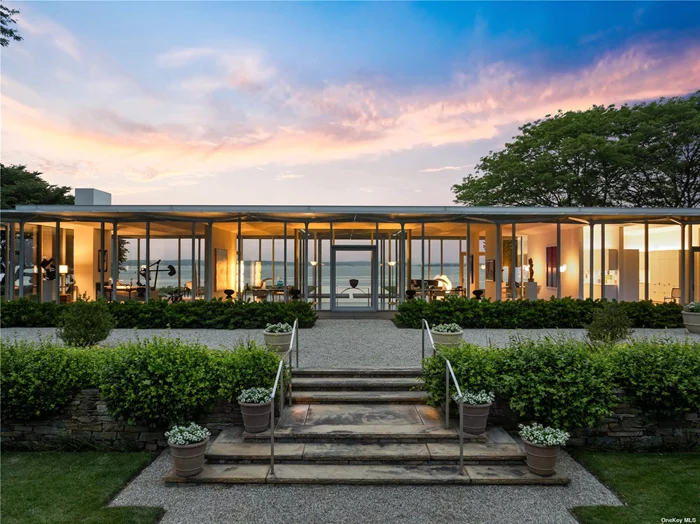 Discover the Glass House. An architectural marvel on Fishers Island, designed by Tom Phifer to blend seamlessly with its lush surroundings. This steel-and-glass home, with unobstructed views of Fishers Island Sound, stands on the site of a former colonial home. The garden, designed by Morgan Wheelock and enhanced by Thomas Armstrong, features vibrant Japanese irises and 150, 000 daffodils. Phifer&rsquo;s design emphasizes transparency, allowing the house to blend into the landscape. The home&rsquo;s steel frame complements the maritime blues and grays of the Sound. A water feature flows through the house, enhancing the connection between the structure and the garden. The primary bedroom, dappled with light, offers views of the meticulously manicured garden. Inside, the house is a masterpiece of minimalism, with walls that don&rsquo;t touch the exterior, creating uninterrupted views. The exterior canopy of aluminum tubes blocks direct sunlight, ensuring comfort and beautiful soft light. The interior features six skylights and minimal doors, emphasizing the peaceful expanse of the space. This property, a sanctuary of art, architecture, and nature, offers a serene retreat on exclusive Fishers Island, accessible only by ferry, boat, or plane. Experience unparalleled living in this harmonious blend of design and natural beauty.