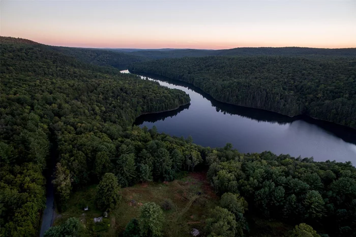 Come build your dream home on one of the very few waterfront parcels on the Rio Reservoir, a protected and pristine 422 acre body of water. A large boulder on the shore makes a perfect spot for an idyllic afternoon swimming in its clear and refreshing water. The vista from the shore will never change, it is protected a DEC bald eagle conservation. Paddle across the reservoir to find a beautiful waterfall. The 4.39 acre lot has a gentle slope off the road with a driveway already in place and a pretty perfect build site. Electric and internet can easily be pulled to the property from nearby utility poles. Two huge, age-wisened maple trees welcome a visitor, and pine, hawthorn, green apple and hickory trees are found lining the lovely open meadow. The two sheds are grandfathered and two more structures may be built per local code.Old stone walls on the property are romantic relics of the Drake Hotel, a rooming house in the late 1800s. There is an existing well on the property that could very likely be serviced and brought back to life. Located in Forestburgh, NY, just a 2 hour drive to the George Washington Bridge, near some of the best darn pizza in the area, Forage Pizza. There is a convenient NJ Transit train at Port Jervis just 20 minutes away. Bethel Woods Center for the Arts is a great venue for summer concerts and just 35 minutes away.