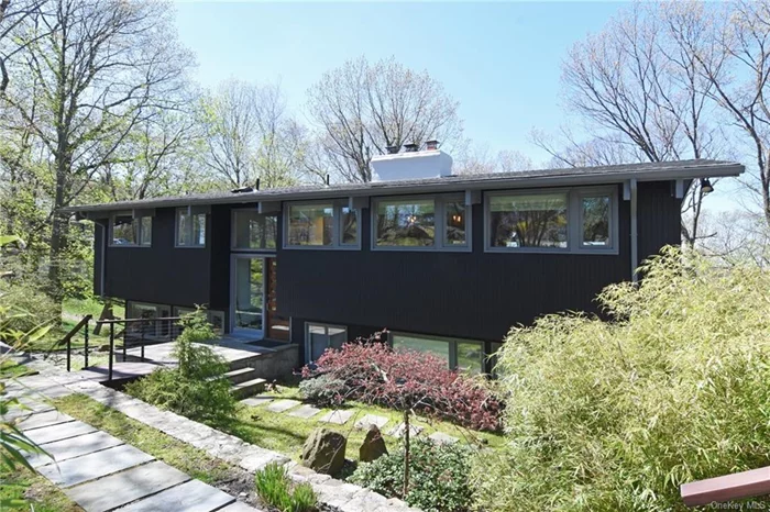 Nestled amongst the trees, this stylish mid-century modern home with expansive multi-level decks, offers seasonal Hudson River views and an unparalleled connection with nature. Located just steps from the Irvington Woods, with 400 acres of forever greenspace, this property is also close to schools, the charming Village of Irvington and the Metro North Train station, ensuring an easy-going lifestyle. High-end finishes and custom-designed accents complement soaring ceilings, walls of windows and two fireplaces. The airy main level boasts an open kitchen, living and dining area in addition to a spacious office/den and a serene primary bedroom suite. The lower level offers three additional bedrooms, another office, and a recreation room with access to the lower-level decks, completing this exceptional family home.
