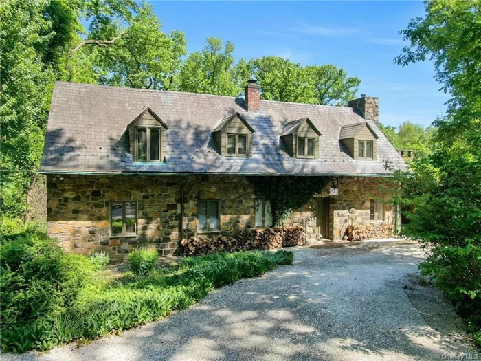 Located in the heart of the Snedens Landing Historic District, this original 1938 home has been thoughtfully renovated to enhance its timeless character and bucolic charm. The property retains its original stone facade and slate roof, while modern touches, including a mid-century style extension, have brought space and light to the residence. The highlight of the home is a bright glass room that is bathed in natural light. From here, glass doors open to a spacious brick patio covered by a trellis draped in mature kiwi vines, creating a serene outdoor space for a shaded al fresco lunch or drinks. The patio overlooks a free-form in-ground pool, which is completely fenced, the contours softened by clematis and climbing hydrangea. The surrounding cottage style gardens are planted with a range of mature specimen trees and a wild profusion of perennial plantings. Drifts of narcissi, grape hyacinth and daffodils surround the gardens in early spring, giving way to peonies and allium in May. There is a raised bed set up for a kitchen vegetable and herb garden. On the edge of the property there is a hand-built treehouse and beyond a fenced area originally used for chickens and other pets. Inside, the home offers an open country kitchen, complete with exposed stone walls and cork flooring. There is a Viking stove/oven and a classic Sub-Zero refrigerator. The kitchen seamlessly flows into a spacious living room with a Russian oak floor featuring a wood-burning fireplace, making it a perfect spot for cozy gatherings. The adjacent dining area is ideal for enjoying casual meals with family and friends. The first floor also includes a small bedroom with a full bath, in addition to a den that can flexibly serve as an office or an additional bedroom, with an adjacent half bath. Progressing to the second floor, a wide landing leads to the primary bedroom with a very generous adjacent full bathroom. A second double bedroom shares this floor, along with another full bath. On the edge of the property is a freestanding garage with a large upstairs studio with a word burning stove and walk in closet. Currently configured as a work from home office suite there is a bathroom/shower on the lower level making it an ideal separate apartment for a nanny or overnight guests. This property is steeped in history, with its location in the Historic District offering a unique connection to the past, particularly the Revolutionary War era. Quaintly described in Historic Houses of Palisades as The House That Jack Built, the architect Wallace Heath has added a creative touch to this home, making it an appealing haven for artists. Former residents include Pinchas Zuckerman and Tuesday Weld. The home is a short walk from the Snedens Landing Tennis Association, the Palisades Free Library, and local favorite, The Filling Station restaurant. The location is excellent for hiking and biking as this private road ends in a trail that leads to the village of Piermont and beyond. Snedens Landing is conveniently located just a 12 mile drive from the George Washington Bridge or a 10-minute drive from the Mario Cuomo Bridge, making it an excellent choice for those who need easy access to the city while enjoying the tranquility of a historic and artistic retreat.