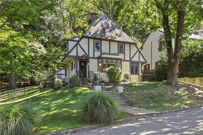 Welcome to this completely charming turnkey home, where classic design meets contemporary convenience.  Step inside the inviting entry to a beautiful living room bathed in natural light, featuring attractive windows and a cozy fireplace adorned with new tile surround. French doors lead to a versatile den/guest room with a full bath, perfect for hosting visitors or creating a serene home office. Flowing seamlessly from the living room, the spacious dining room offers lovely views of the backyard and easy access to the patio through another set of French doors, ideal for indoor-outdoor entertaining. The welcoming kitchen features generously proportioned cabinetry and stainless steel appliances, and provides convenient access to both the rear yard & lower level. Once upstairs, you will find a primary bedroom with double closets and a sweet alcove for desk or armoire. Two additional spacious bedrooms and a full bathroom complete this level. The unfinished attic with higher roof line allows for ample storage. The large lower level adds extra space for storage, laundry and recreation. Step outside to enjoy the patio with area for built-in bbq, perfect for relaxing or hosting gatherings. The professionally landscaped, fenced property is picturesque in all seasons. A sturdy outbuilding can house all of your gardening tools, summer furniture and more. This stylish Tudor provides a perfect setting for comfortable living and gracious entertaining. Walkable to town, library and park. Award winning Ardsley school District. Star reduction if eligible is $1562.