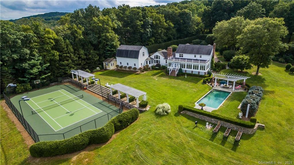 Set back on 9+ acres, this property offers privacy in a choice location. As visitors ease down its circular stone drive the New England Colonial charm of this exceptional estate welcomes them. Upon entering the formal foyer the homes texture and character are made obvious by the wooden wall cladding, a detail that is carried throughout much of the home. The space on the main level is arranged in such a way that there is a sense of ease in movement. Wide, open doorways carry you from one room to the next, while the warmth of the wood paneling creates a sense of intimacy in each individual space. The formal living room and kitchen are open to the homes expansive four-season porch, overlooking the breathtaking views of the Litchfield hills. A large open dining/living area with built-in custom cabinetry abuts the L shaped kitchen workspace. Adjoining is a formal library/office that extends into the illuminated den. On the upper floor there are two bedrooms and two bathrooms. The current (original) owners personalized this living level by converting the third bedroom into an opulent bath & dressing room. Luxurious living extends to the exterior of the home as well, where both sport and relaxation can be found in the homes gunite pool and tennis court. With mature plantings throughout and expansive views the properties landscape rings true to the title of country estate.