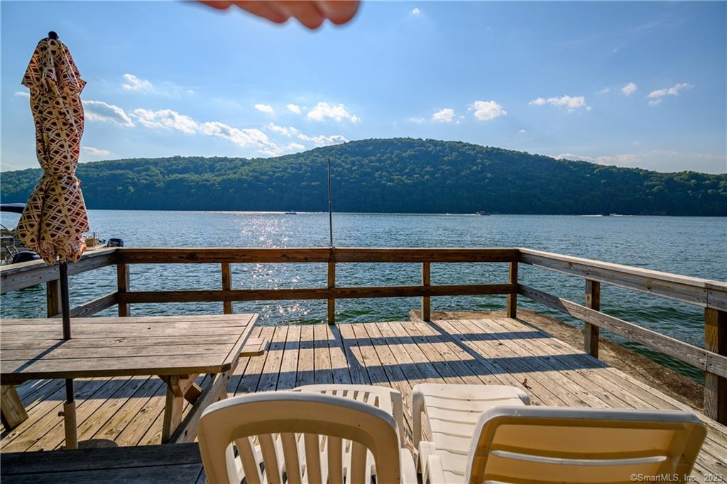 Nature's Beauty abounds in this Tucked-away Direct Lakefront 4BR / 3 Bath Home. Set proudly on half-acre hillside that harkens back to easier times, where you can go for a swim, lie in the hammock, play cards on the deck & remember to just breathe. Unmatched Seasonal Views that frame beloved Candlewood Lake. Spring & Summer offer private mornings serene, fall sunsets from massive wrap around deck where you can unpack just picked apples from the farm among stunning foliage, or perhaps the best are Winter Snow dusted Pines w lake backdrop viewed while you sit by the grand double-sided floor to ceiling Stone Fireplace set ablaze to warm the spirit, perfect for the holidays.50 ft of Direct Waterfront w private dock/deck facing protected Bear Mountain Land Preserve. Gigantic Eat-In-Kit w Huge Pantry. Versatile Front Room/DR features Fireplace & New Flooring. Covered Wrap around Deck w Ceiling Fans is Fantastico! Dining al fresco was never better & the best place to be during a summer rain or a winter snowfall. Upper Level Features a Large 2nd FR for gathering. Primary BR designed to become 2 bedrooms if you wish. 2 add'l. BRs offer plenty of space. Recent updates include: New Beautifully Done Stairs to Lake w Hand Rail. New Exterior Siding, Trim & Gutters. New Handsome & Purposeful Retaining Wall behind home. Newer Range, DW, Some Plumbing, Fixtures, LR & DR Flooring. Ample Parking, Garage & Plenty of Storage. 70 Min. to NYC. The raw serenity will grab hold, escape is yours!